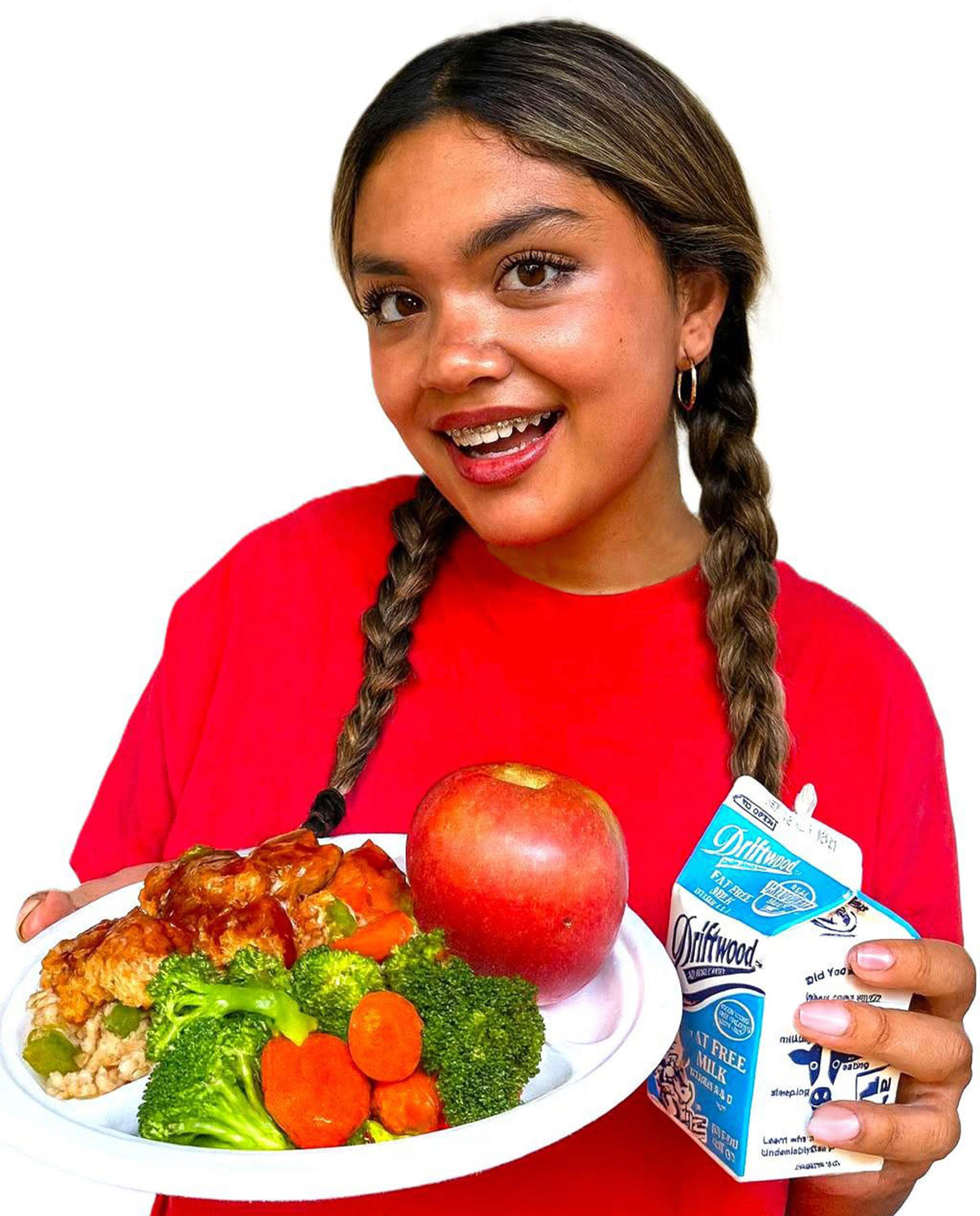 Young girl in a red shirt holding a plate of chicken with an apple and side of mixed vegetables and also holding a carton of milk Young girl in a red shirt holding a plate of chicken with an apple and side of mixed vegetables and also holding a carton of milk